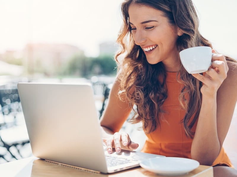 woman on her laptop at a cafe drinking coffee outdoors