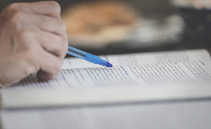 hand_holding_pen_studying_with_textbook_daylight_macros