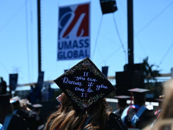graduate cap with UMass Global sign in the background