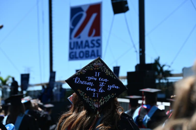 graduate cap with UMass Global sign in the background