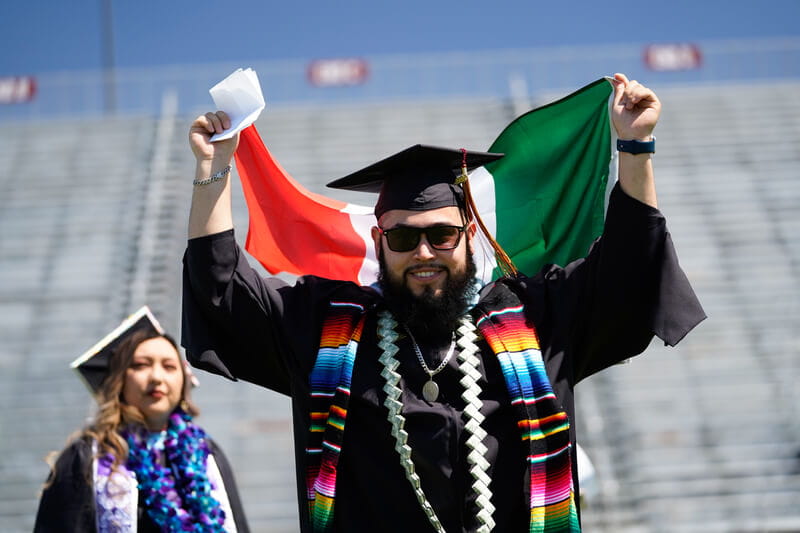 male_student_cap_and_gown_thumbs_up_at_commencement