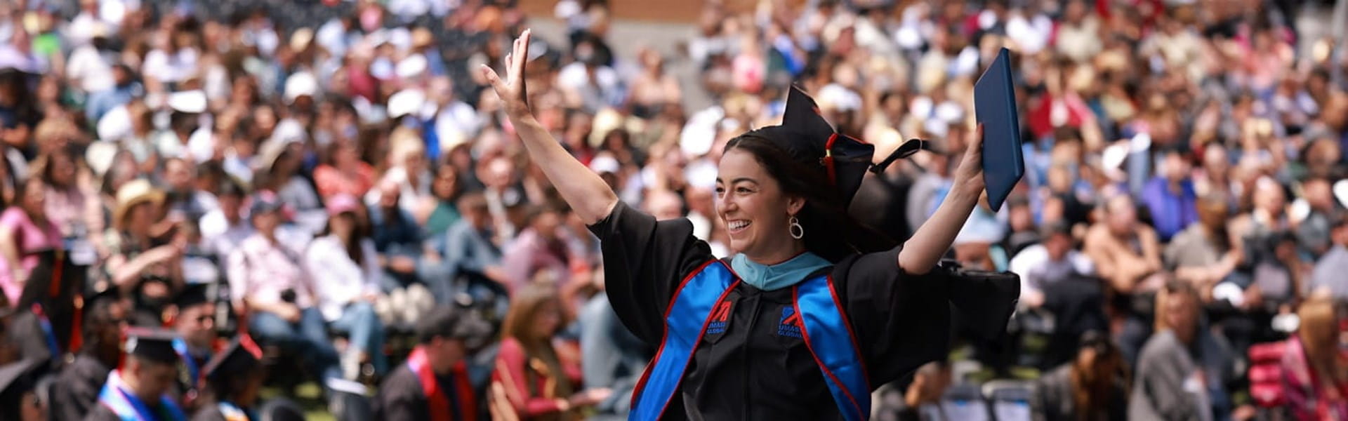 female graduating from UMass Global and waiving to audience
