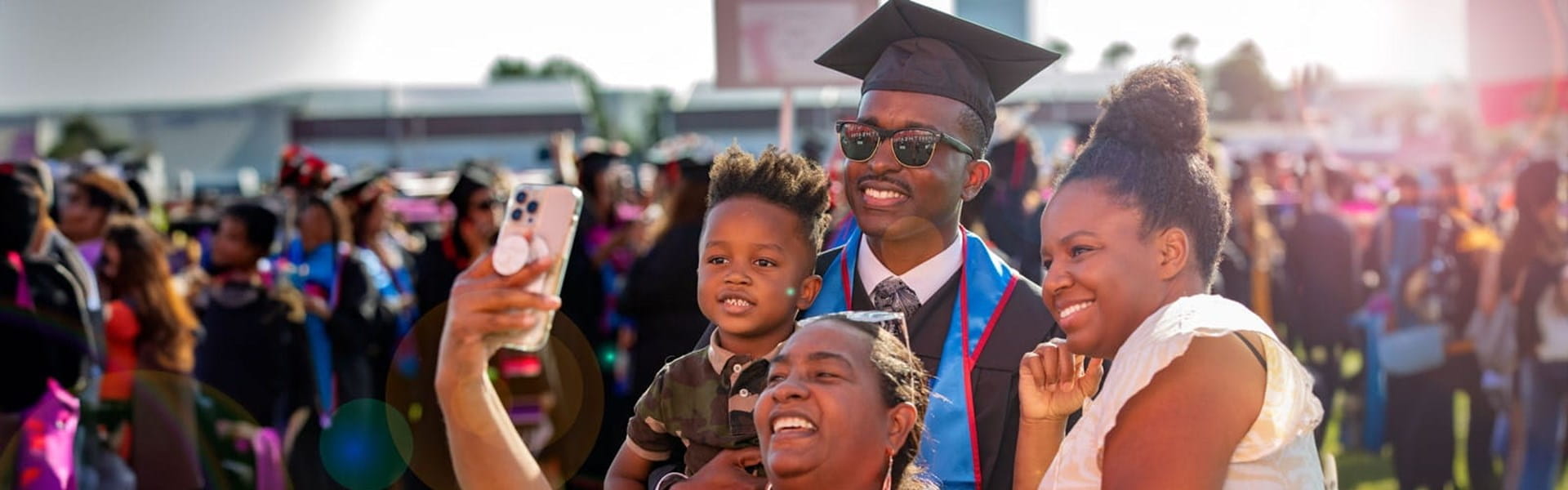 male UMass Global graduate at commencement taking a selfie with his family