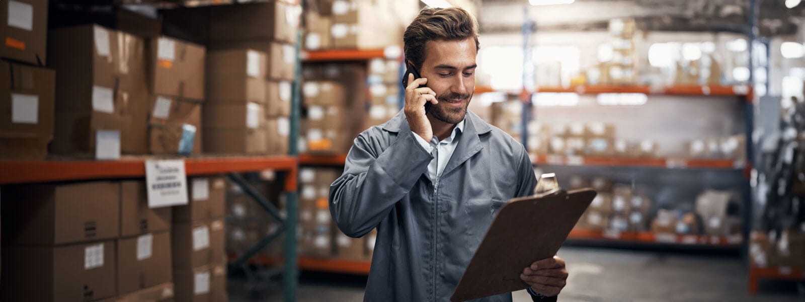 male manager in a jumpsuit looking at an inventory supply list in a warehouse