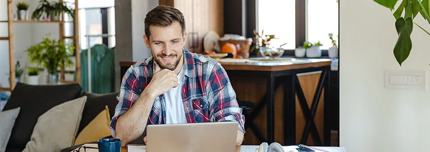 a male happily looking at his laptop in his living room