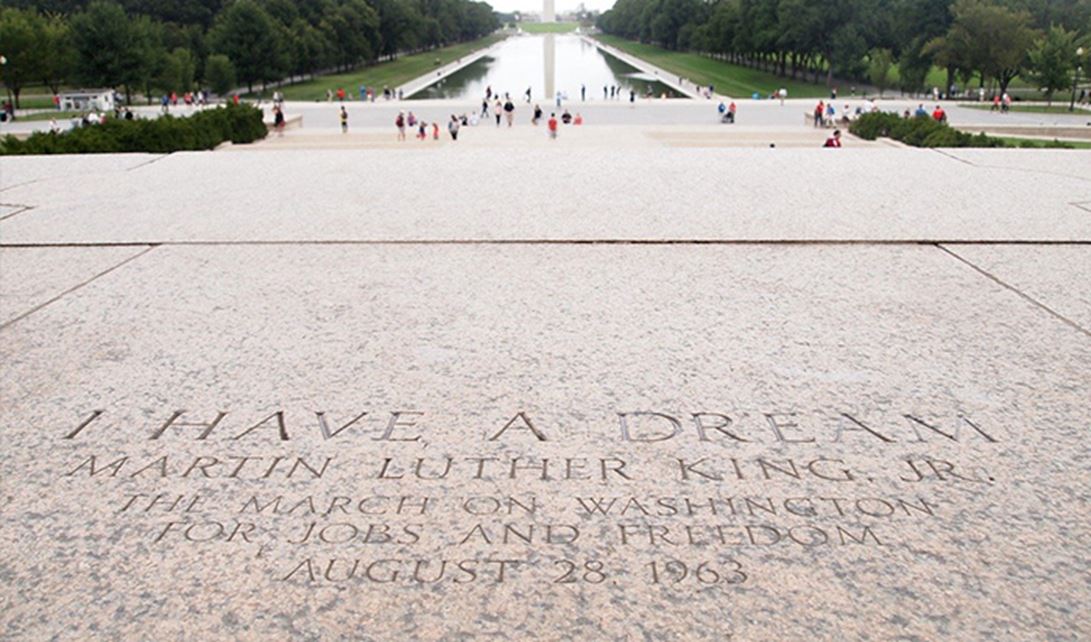 The words of Martin Luther King Jr.'s "I Have a Dream" speech carved in stone with the Lincoln Memorial Reflecting Pool and Washington Monument in the background.