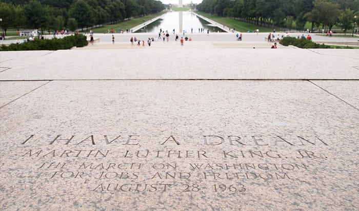 The words of Martin Luther King Jr.'s "I Have a Dream" speech carved in stone with the Lincoln Memorial Reflecting Pool and Washington Monument in the background.