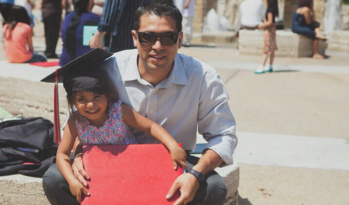 A graduate with his daughter, who is wearing his graduation cap