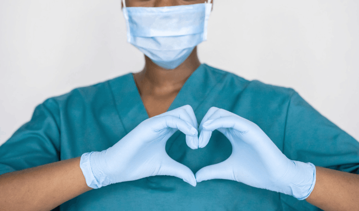 A healthcare worker wearing scrubs and making a heart shape with their hands.