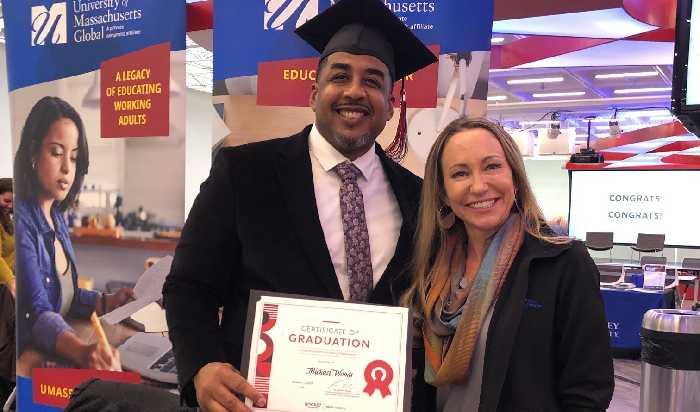 Rock Academy Graduate Michael Woods, wearing graduation regalia, stands next to Michelle Goyette of UMass Global. 