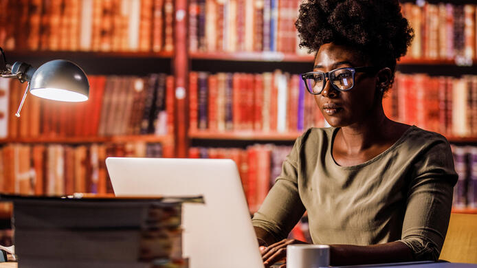 Young woman using laptop, sitting at desk in a library.