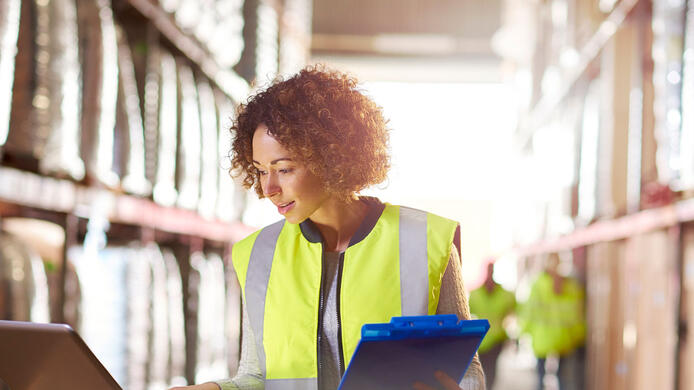 a female warehouse manager looks at her stock on a laptop checking her delivery sheet in the warehouse .
