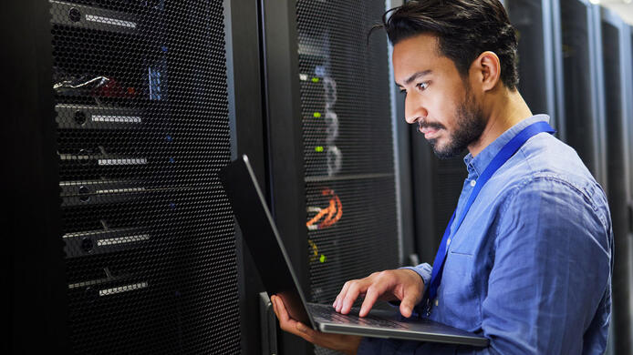 Programming, data center and a man with a laptop for maintenance, cyber security and internet check. Coding, email and an Asian programmer typing on a computer for network or server analytics