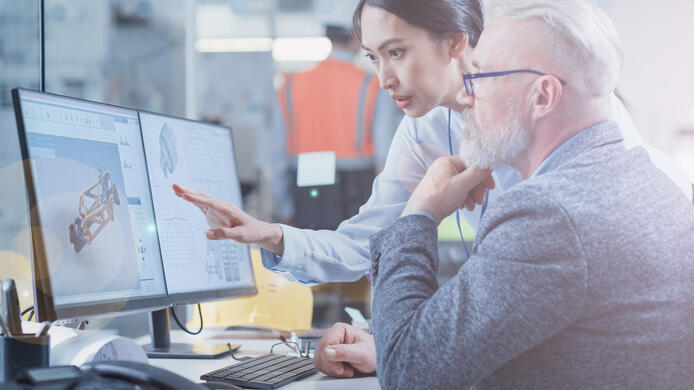 Factory Office Facility: Industrial Engineers Drafting Blueprints of a Heavy Industry Machine Parts on a Computer CAD Software. Asian Female Technician Discusses Work with Middle Aged Designer.