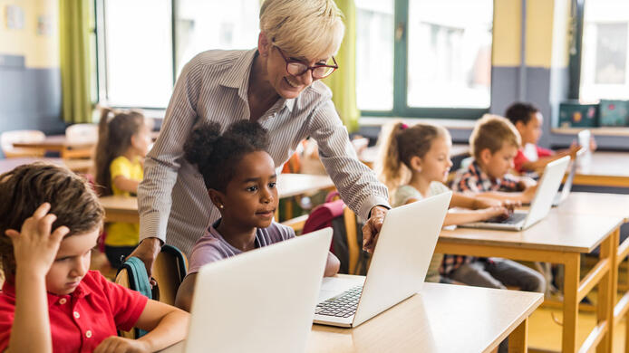 Happy female teacher assisting school kids during an e-learning class at elementary school.