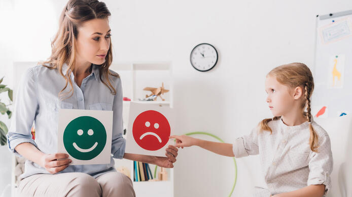 adult psychologist showing happy and sad emotion faces cards to child