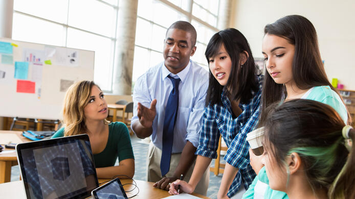 Diverse group of creative graphic designers discuss their project in modern office. The group consists of a mid-adult African American male, Asian female and Hispanic females.
