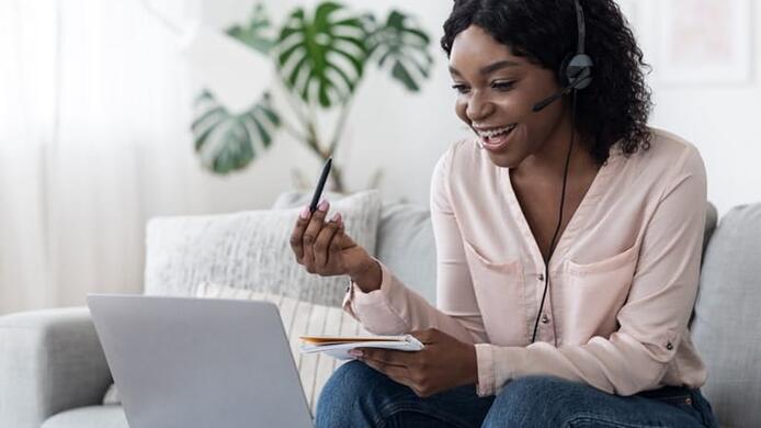 young female student interacting on laptop with headset on