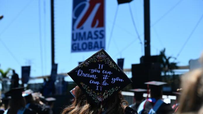 graduate cap with UMass Global sign in the background