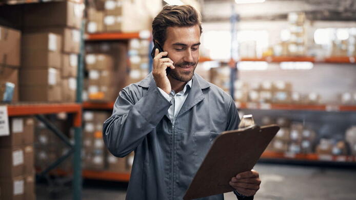 male manager in a jumpsuit looking at an inventory supply list in a warehouse
