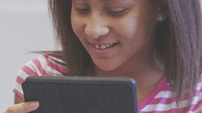 female pre k - 12 teacher helping a young female student on her tablet in classroom