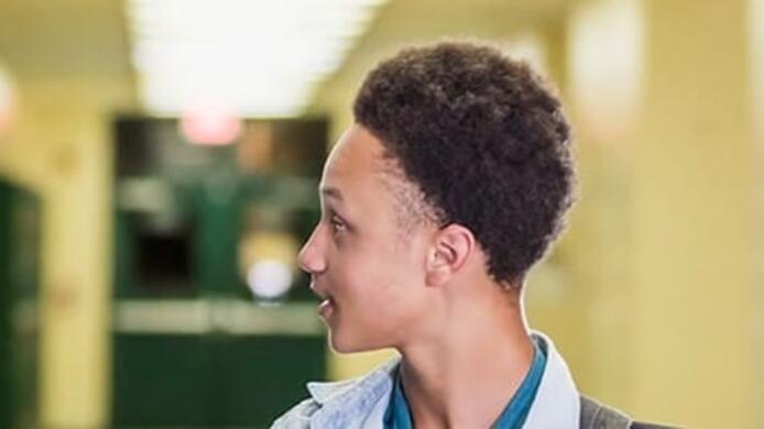 male school counselor supporting  male student walking through school halls by locker
