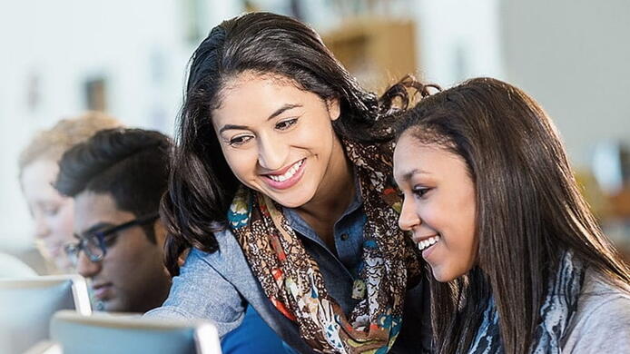 High school teacher assisting a student at a computer.