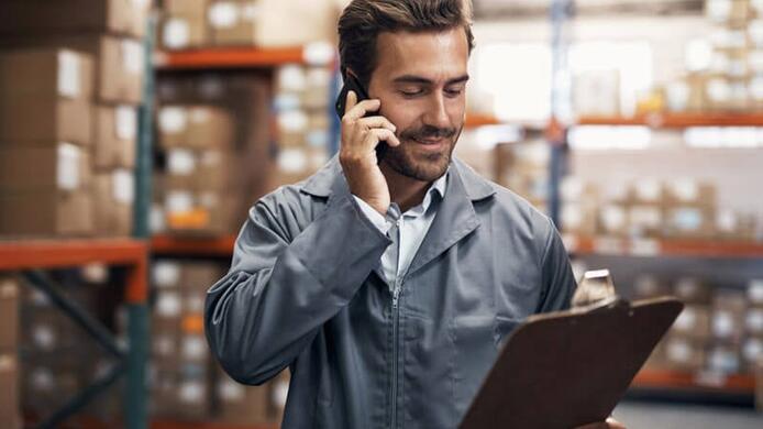 male manager in a jumpsuit looking at an inventory supply list in a warehouse