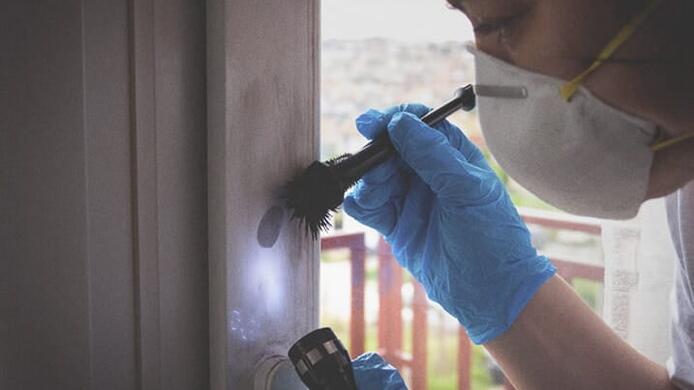 female forensic investigator examining evidence on wall with gloves and flashlight