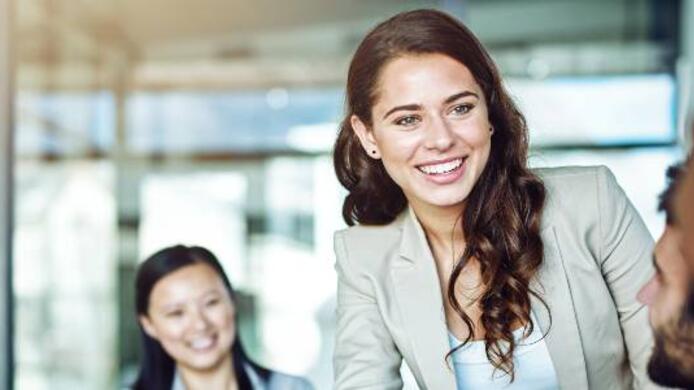 two women and 1 man in suits smiling to a man