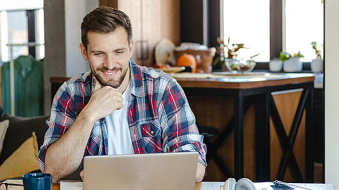 a male happily looking at his laptop in his living room