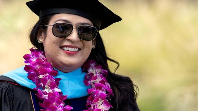 A photo of 2022 UMass Global graduate Melinda Gonzalez wearing academic regalia and a purple lei.