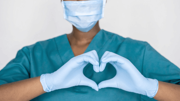 A healthcare worker wearing scrubs and making a heart shape with their hands.