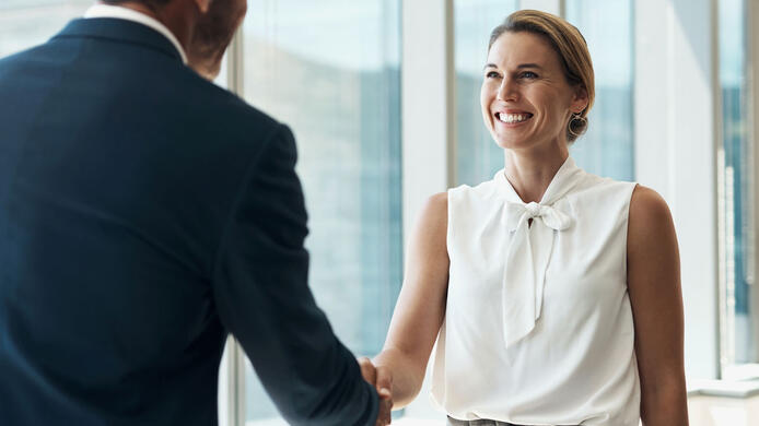 two businesspeople shaking hands in a corporate setting.