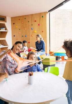 Happy Latin American teacher having fun with her students playing with slime at the school - elementary education concepts