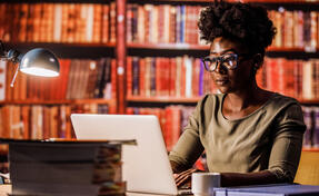 Young woman using laptop, sitting at desk in a library.