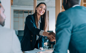 Business people shaking hands in the office. Group of business persons in business meeting. Three entrepreneurs on meeting in board room. Corporate business team on meeting in modern office. Female manager discussing new project with her colleagues. Company owner on a meeting with two of her employees in her office.