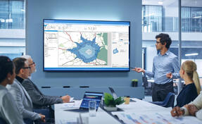 Office Conference Room Meeting Presentation: Latin Businessman Talks, Uses Wall TV to Show Company Growth with Big Data Analysis, Graphs, Charts, Infographics. Multi-Ethnic e-Commerce Startup Workers