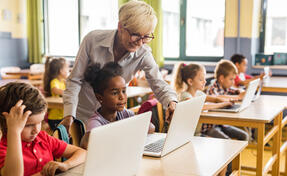 Happy female teacher assisting school kids during an e-learning class at elementary school.