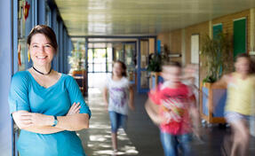 Portrait of a smiling elementary school teacher with running children in the school corridor