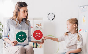 adult psychologist showing happy and sad emotion faces cards to child