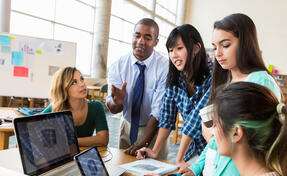 Diverse group of creative graphic designers discuss their project in modern office. The group consists of a mid-adult African American male, Asian female and Hispanic females.