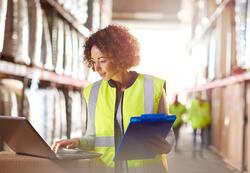 a female warehouse manager looks at her stock on a laptop checking her delivery sheet in the warehouse .