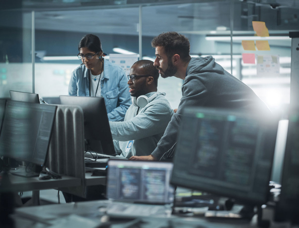 Team of three techs discussing and looking at computer monitors