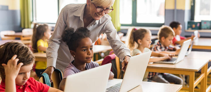 Happy female teacher assisting school kids during an e-learning class at elementary school.