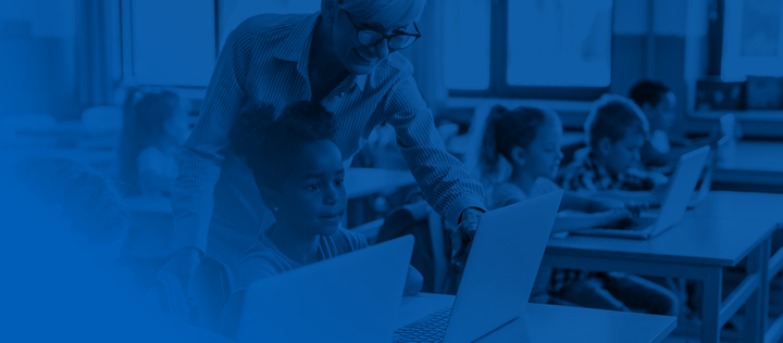 Happy female teacher assisting school kids during an e-learning class at elementary school.
