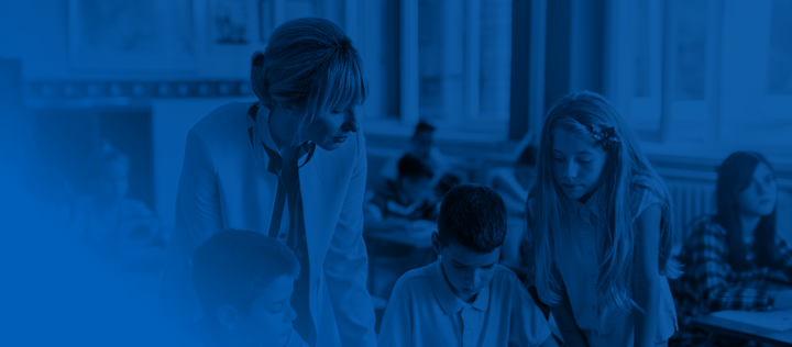 Mid adult teacher helping group of school children with learning in the classroom.