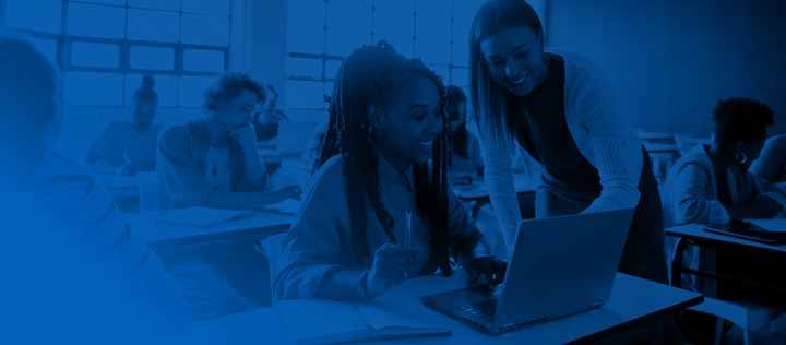 Smiling young female teacher helping a student working on a laptop during a lesson in a school classroom