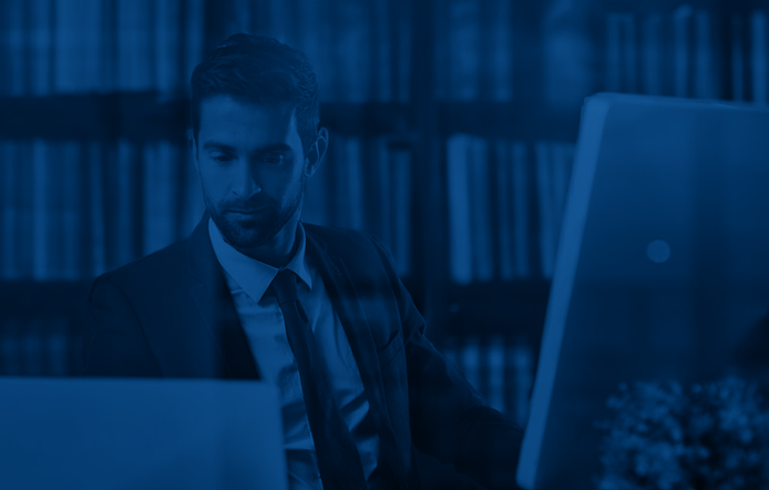 man working on a computer in a paralegal job with books behind him