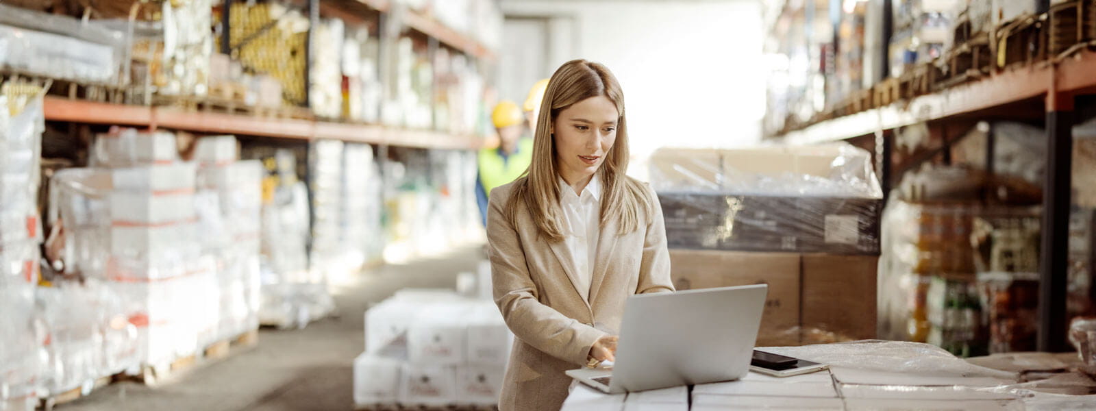 female in a business suite working in a warehouse looking at inventory on her computer